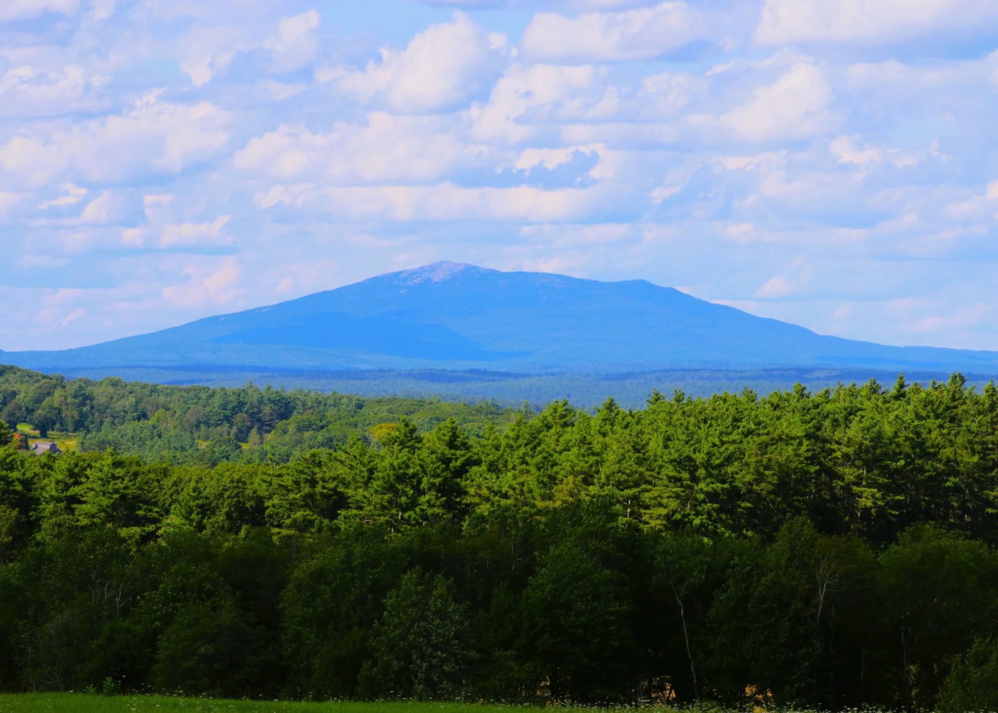 Image of Mount Monadnock with partly cloudy sky and trees below